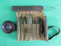 Full view of the open leather roll-up case showing multiple straight razors and sharpening strap on green background