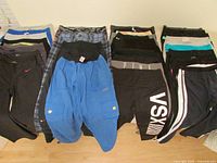 Top-down view of folded pants laid out in three rows showing variety of colors and styles including black, blue, and patterned pants