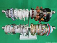 Full view of two-tier bracelet stand filled with assorted bracelets of various styles and materials on green background.