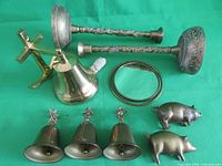 Photo showing all lot items arranged on green background, includes candlesticks, bells, pig figurines, cross, handbell, and oval mirror frame.