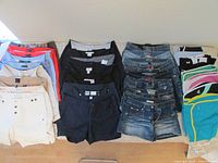 Full lot view showing all 25 pairs of shorts laid out on a bed, sorted by type and color including denim, athletic and casual.
