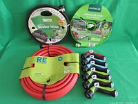 Photo shows three garden hoses: red Room Essentials brand, green Gardenline sprinkler hose, black Swan soaker hose plus six assorted spray heads with black and blue grips.