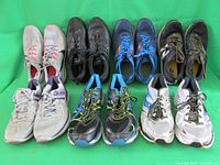 Front view of 7 pairs of men's sneakers arranged in two rows on a green background
