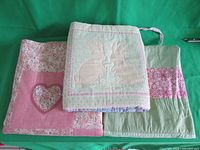 Photo of three folded quilts with pastel colors including pink, green, and lavender. Shows rabbit applique and heart applique designs.