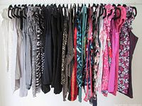 Wide view of the sleeveless tops hanging on a rack showing a gradient from neutral tones to vibrant pinks and floral prints.
