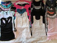 Photo showing a large variety of women's summer tanks and sleeveless tops in multiple colors and styles arranged on a bed.