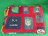 Folded quilt resting on a green background showing multiple embroidered patches on denim squares bordered by red fabric.
