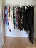 Photo showing a selection of women's tops and dresses on hangers; various colors, patterns including floral and polka dots, mostly small and medium sizes