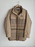 Front view of beige and multi-colored stripe Patagonia jacket hanging on wooden hanger against white wall