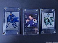 Three hockey cards in clear metal-screwed protective holders showing front artwork of players Mats Sundin (Toronto Maple Leafs), a second Leafs player, and a Dallas Stars goalie.