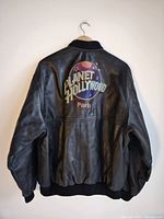 Back view of black leather jacket showing large embroidered Planet Hollywood Paris logo with colorful globe design.