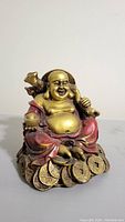 Front view of Laughing Buddha figurine showing joyful facial expression, gold and red details, seated on pile of gold coins