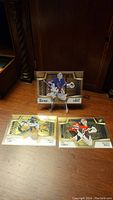 Three gold-themed NHL goalie cards arranged on a wood surface with one on a stand.