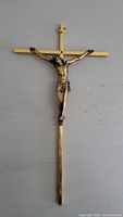 Full front view of a metal crucifix showing the gold cross and bronze Jesus figure on it against a gray background.
