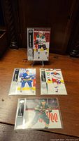 Four hockey rookie and first year cards displayed on a wooden table with one card standing on a small display stand.