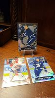 Three hockey cards displayed on a wooden surface including Tim Horton, Austin Matthews, and Cole Cofield cards.