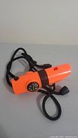 Orange whistle flashlight laying on a flat surface showing compass and thermometer.