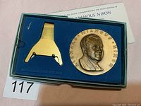 Bronze medal with relief portrait of Richard Nixon in blue-lined box, including gold-colored stand and certificate.