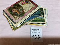 Top view of a stack of approximately 60 postcards featuring a colorful vintage card showing a romantic scene inside a heart shaped frame with floral borders and an inscription.