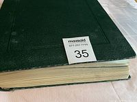 Closed green hardcover stamp album on a table with auction lot number 35.
