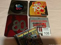 Five CDs displayed on white surface: Hits of the 60s, Hits of the 70s, 80 Hits, Punk Rock Jukebox, and Survival of the Fittest audiobook