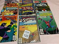 Front view of 14 comic books arranged in three rows, showing titles and cover art including Marvel Fanfare, Justice, Green Lantern, Cloak, Daredevil, Superman, Batman, Spider-Man.
