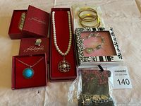 Image of costume jewelry items grouped on a beige fabric surface including boxed necklaces, bracelets, and earrings.
