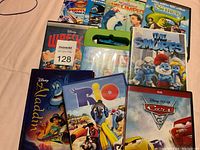 Nine DVD movies displayed on a surface showing titles including Aladdin, Rio, Cars 2, The Smurfs, Shrek, The Incredible Mr. Limpet, and others.