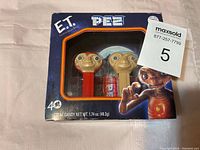 Two E.T. PEZ dispensers in original 40th anniversary packaging with candy packs visible inside the box. Packaging has E.T. themed graphics and clear window showing dispensers.