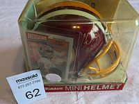 Photo showing the signed mini helmet encased in clear plastic display with Gary Clark's NFL trading card visible behind it, along with auction tag number.