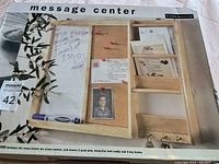 Photo of message center front showing dry erase board section, cork board with push pins, mail caddy, and key hooks, in original box with slight box damage visible.
