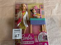Barbie doll in packaging alongside baby doll and medical accessories, front view