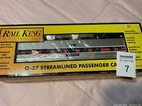 Photo of the Rail King O-27 Streamlined Passenger Car in original yellow package showing side of passenger car with red, white, and blue stripes and detailed model features.