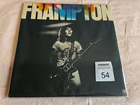 Front cover of the used vinyl album featuring Peter Frampton playing guitar with 'FRAMPTON' in colorful letters above.
