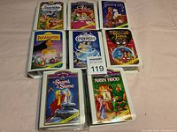 Photo showing set of 8 Walt Disney Masterpiece Collection VHS tapes laid out in two rows on a pink surface. Includes Snow White, Alice in Wonderland, The Aristocats, Pocahontas, Cinderella, Return of Jafar, Sword in the Stone, and Robin Hood (opened).