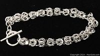 Full view of the sterling silver bracelet with intricate interlocking links and a toggle clasp, placed against a black background.