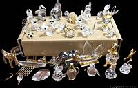 Photo showing assortment of clear glass and crystal miniatures including animals, a perfume bottle, a small swan boat, and decorative pieces with some gold-tone metal accents.