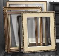 Photo showing six old picture frames of various gold and brown tones and styles leaning against a wall on the floor.
