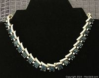 Full view of the blue and clear stone evening necklace on a black display stand, showing necklace length and overall design.