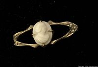 Front view of small cameo brooch showing the white carved profile cameo set in gold frame with floral accents.