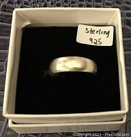Front view of sterling silver ring inside box showing smooth band and sticker marked 'Sterling 925'.