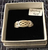 Top view of sterling silver ring with raised Celtic knot design inside a display box with black velvet lining and a label reading "sterling 925".