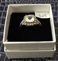 Front angled view of sterling silver ring with large clear square faceted stone surrounded by small round clear stones in black box with 925 tag