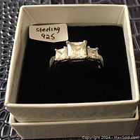 Sterling silver ring with three clear stones in a white jewelry box. Front view showing stone setting and size tag.