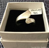 Sterling silver ring in white box with black interior, showing unique curved design and wear marks.