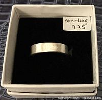 Top view of silver ring in box showing engraving "YOU & ME" with label saying sterling 925.