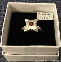 Top view of sterling silver ring with star design and central red stone in box
