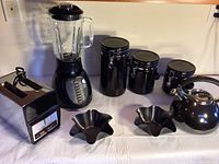 Blender, toaster, three ceramic canisters, two black wavy bowls and black teapot arranged on table
