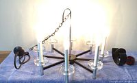 Photo of black metal chandelier with faux candles and three black metal candle sconces on a towel-covered surface, showing the chain and arms of the chandelier.