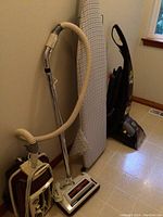 Vintage Eureka canister vacuum with hose, metal wand, and roller brushes, showing duct tape repair.